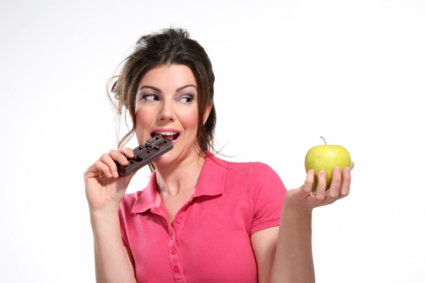 Женщина ест шоколад и держит яблоко - фото
