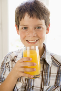 Ребенок широко улыбается и держит в руках стакан сока