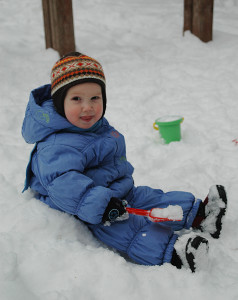 Маленький ребенок сидит в снежном сугробе - фото