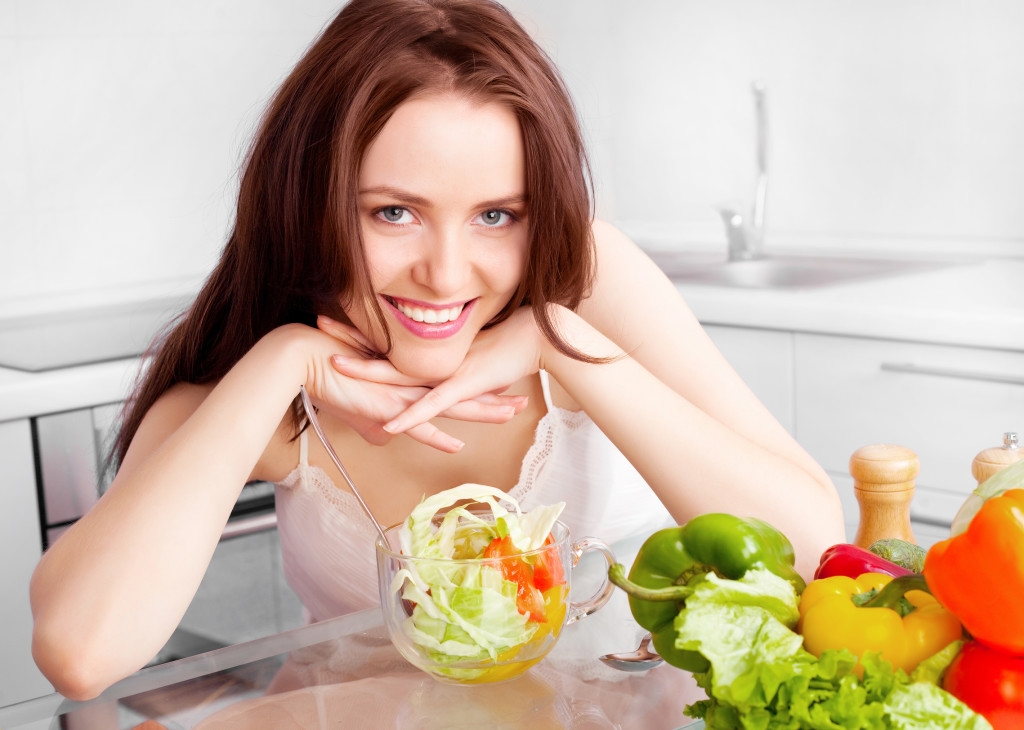 Женщина сидит за столом, свежие овощи - фото