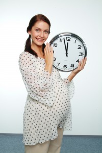 Беременная держит в руках большие часы - фото