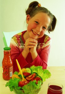Девочка перед обеденным столом, на столе салат из овощей - фото