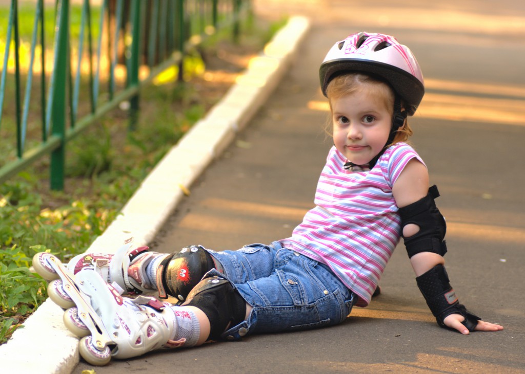 Ребенок в роликах и шлеме сидит на дороге
