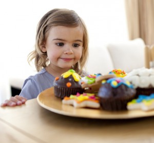 Маленькая девочка смотрит на тарелку с пирожными - фото