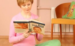 Беременная читает книгу, сидя на полу - фото
