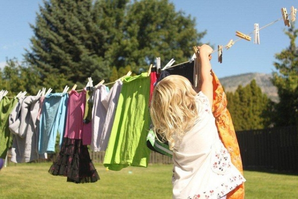 Маленькая девочка развешивает мокрую одежду - фото