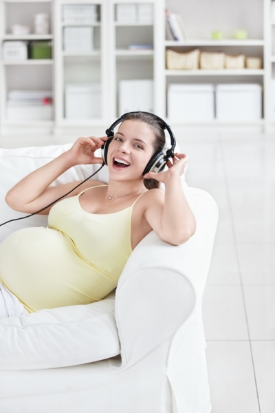 Беременная слушает музыку в наушниках - фото