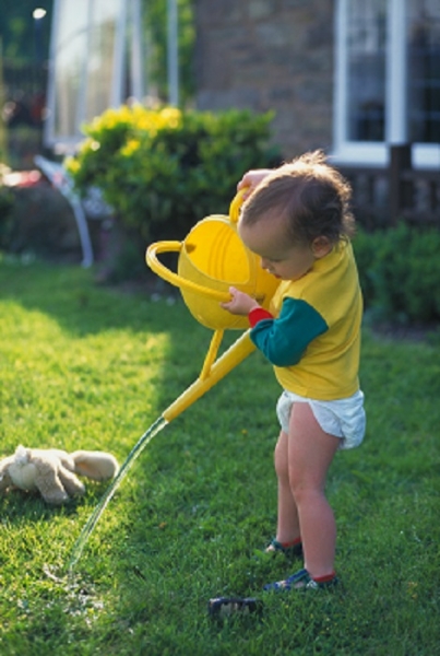 Малыш поливает лужайку из лейки - фото