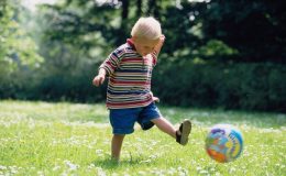 Маленький хлопчик грає з м'ячем на галявині.