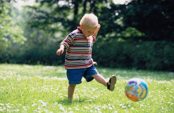 Маленький мальчик играет с мячом на лужайке - фото