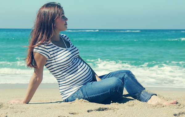 Беременная сидит на пляже возле моря - фото
