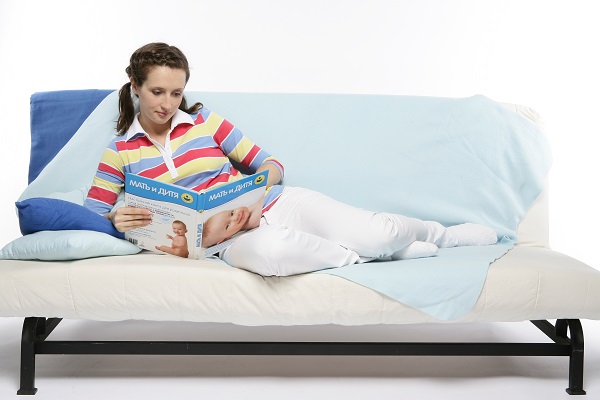 Беременная читает, лежа на диване - фото