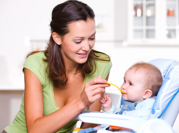 Mother feeding hungry baby in the highchair indoors